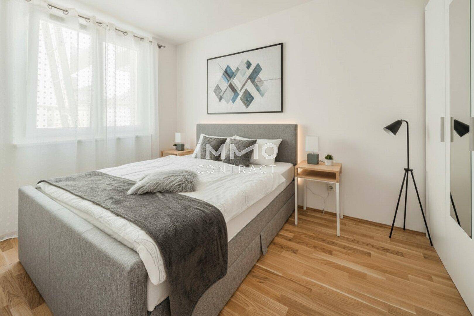 Gemütliches Schlafzimmer mit hellem Parkettboden, großem Fenster und modernem Doppelbett.