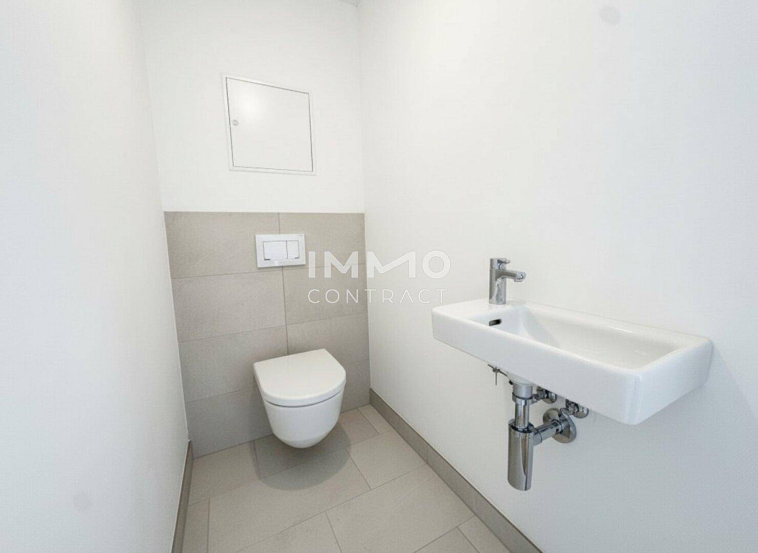 Kompaktes Gäste-WC mit Wand-WC, kleinem Waschbecken und hellen Fliesen an der Wand.