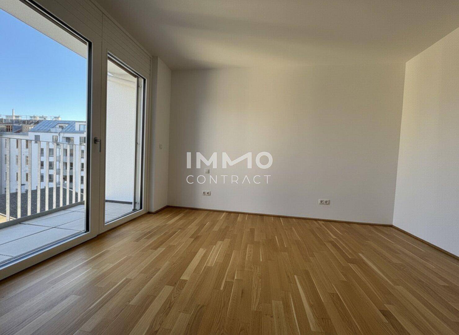 Heller Raum mit Parkettboden und großem Fenster mit Zugang zu einem Balkon.