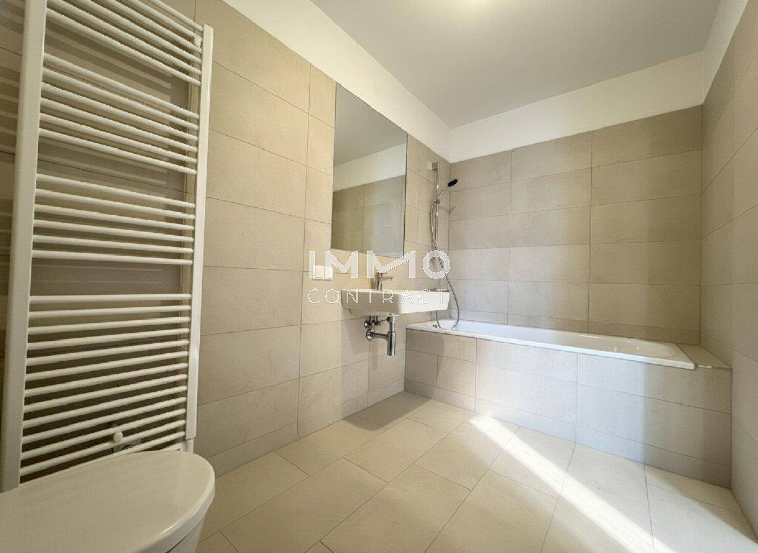Modernes Badezimmer mit beigefarbenen Fliesen, Badewanne und beheiztem Handtuchhalter.