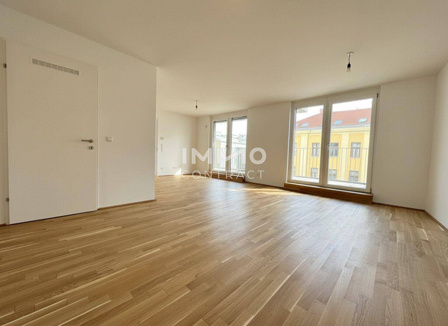Geräumiger Wohnbereich mit hellem Parkettboden und Zugang zu einem französischen Balkon.