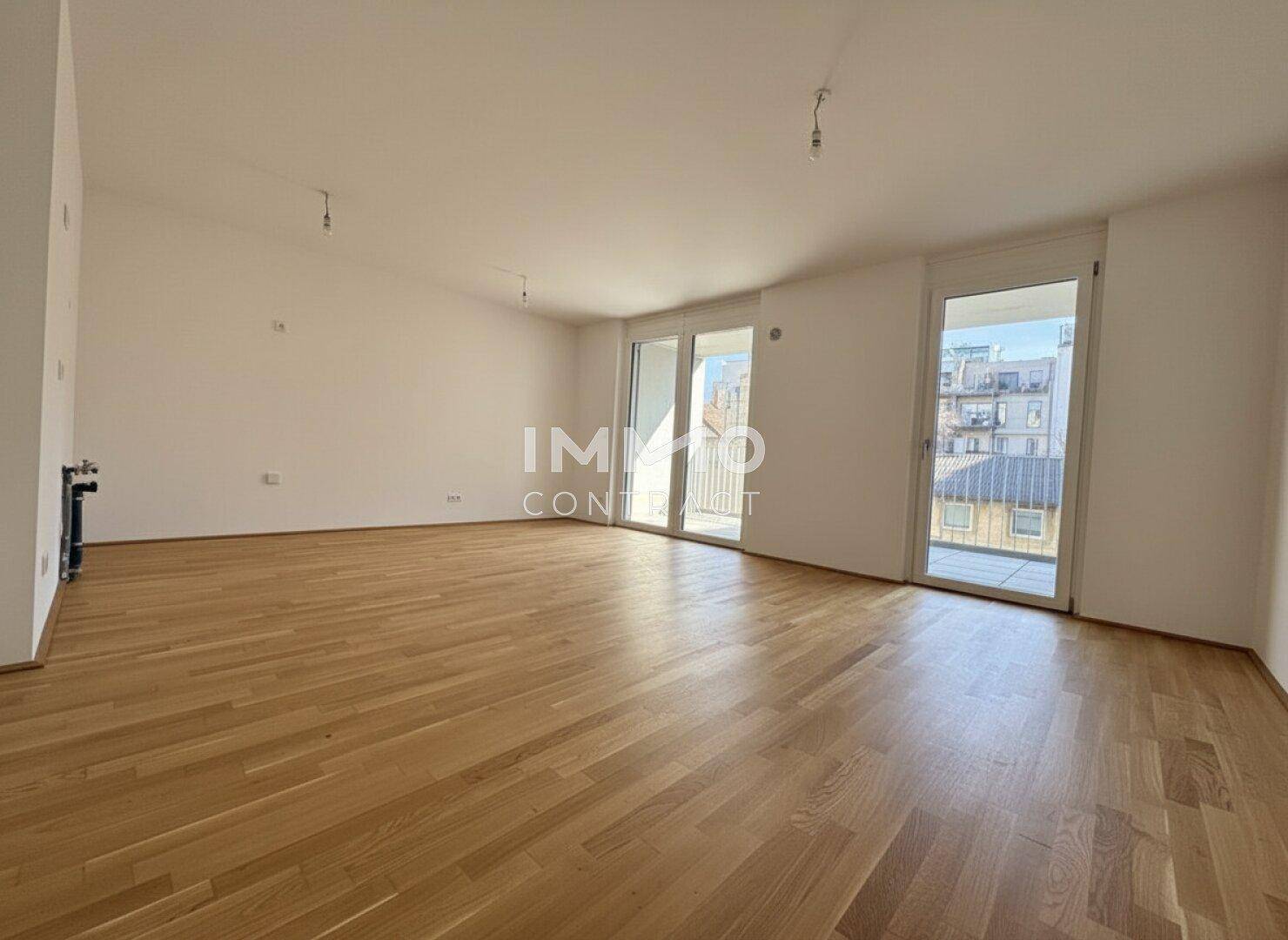 Geräumiges, leeres Wohnzimmer mit Holzboden und Zugang zu zwei Balkonen.