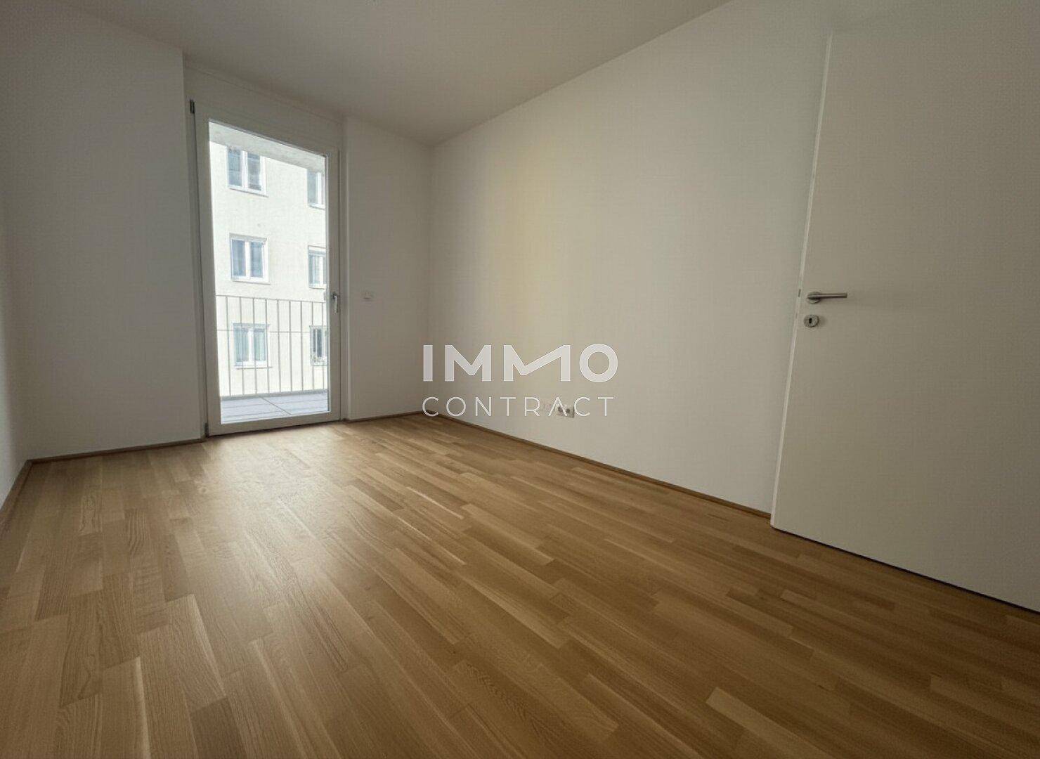 Leeres Schlafzimmer mit Holzboden und direktem Zugang zum Balkon.