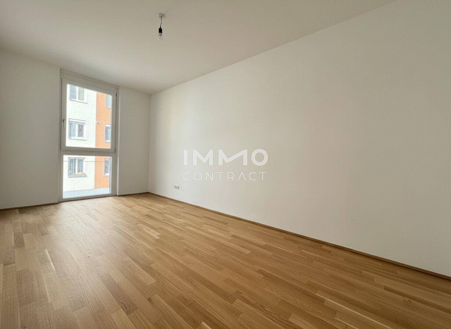 Geräumiges, leeres Schlafzimmer mit Holzboden und großem Fenster.