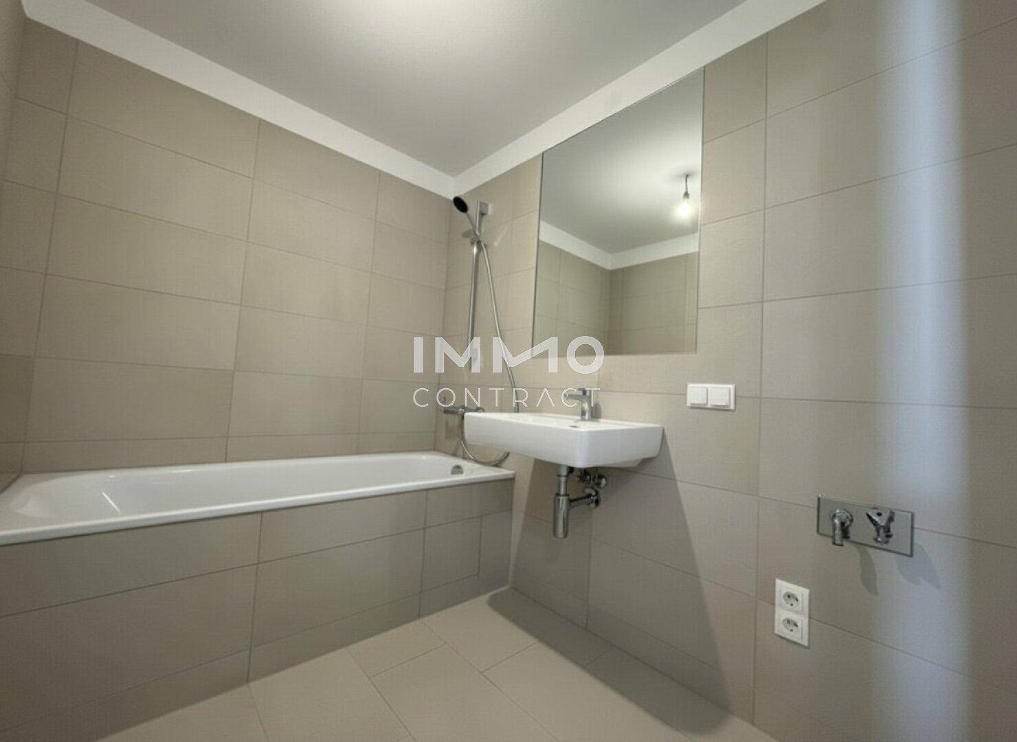 Modernes Badezimmer mit Badewanne, Dusche und großem Spiegel, in hellen Fliesen gehalten.
