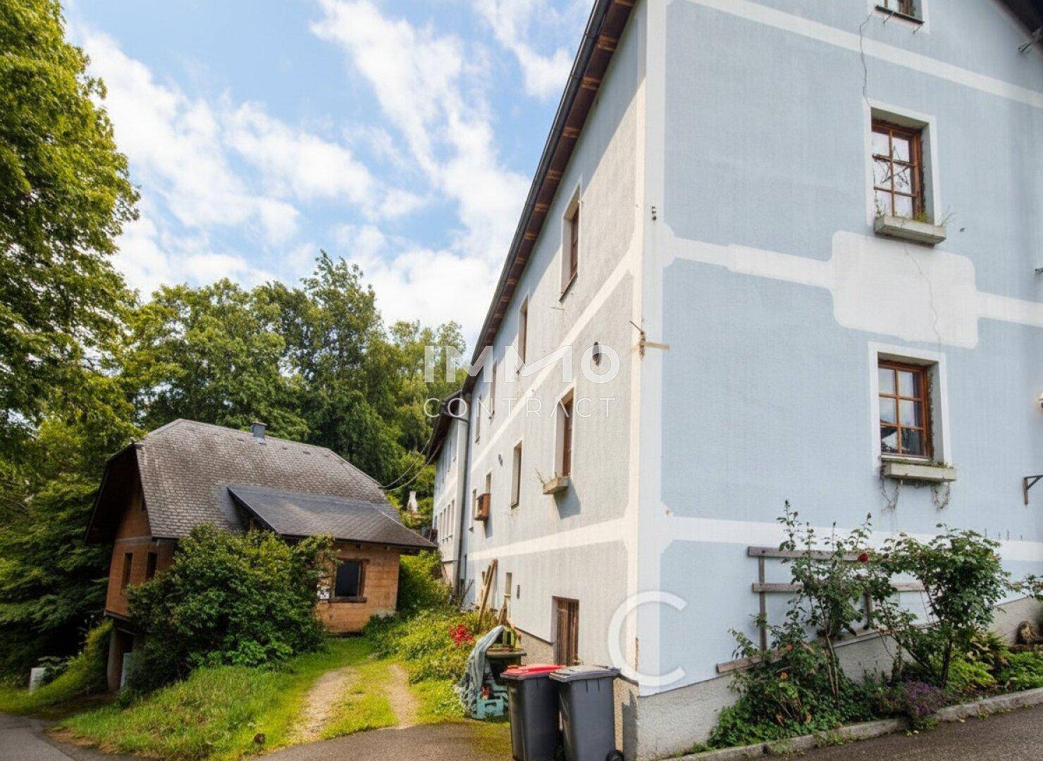 Seitenansicht des historischen Gebäudes mit angrenzendem Nebengebäude und ländlicher Umgebung.