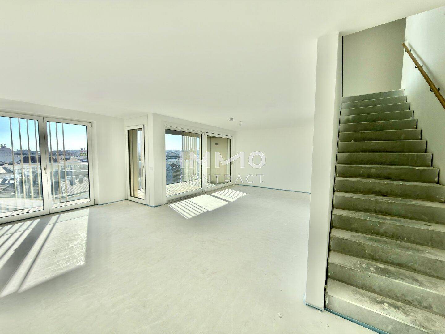 Heller, unmöblierter Wohnbereich mit Treppe und großen Fenstern, die viel Tageslicht hereinlassen.