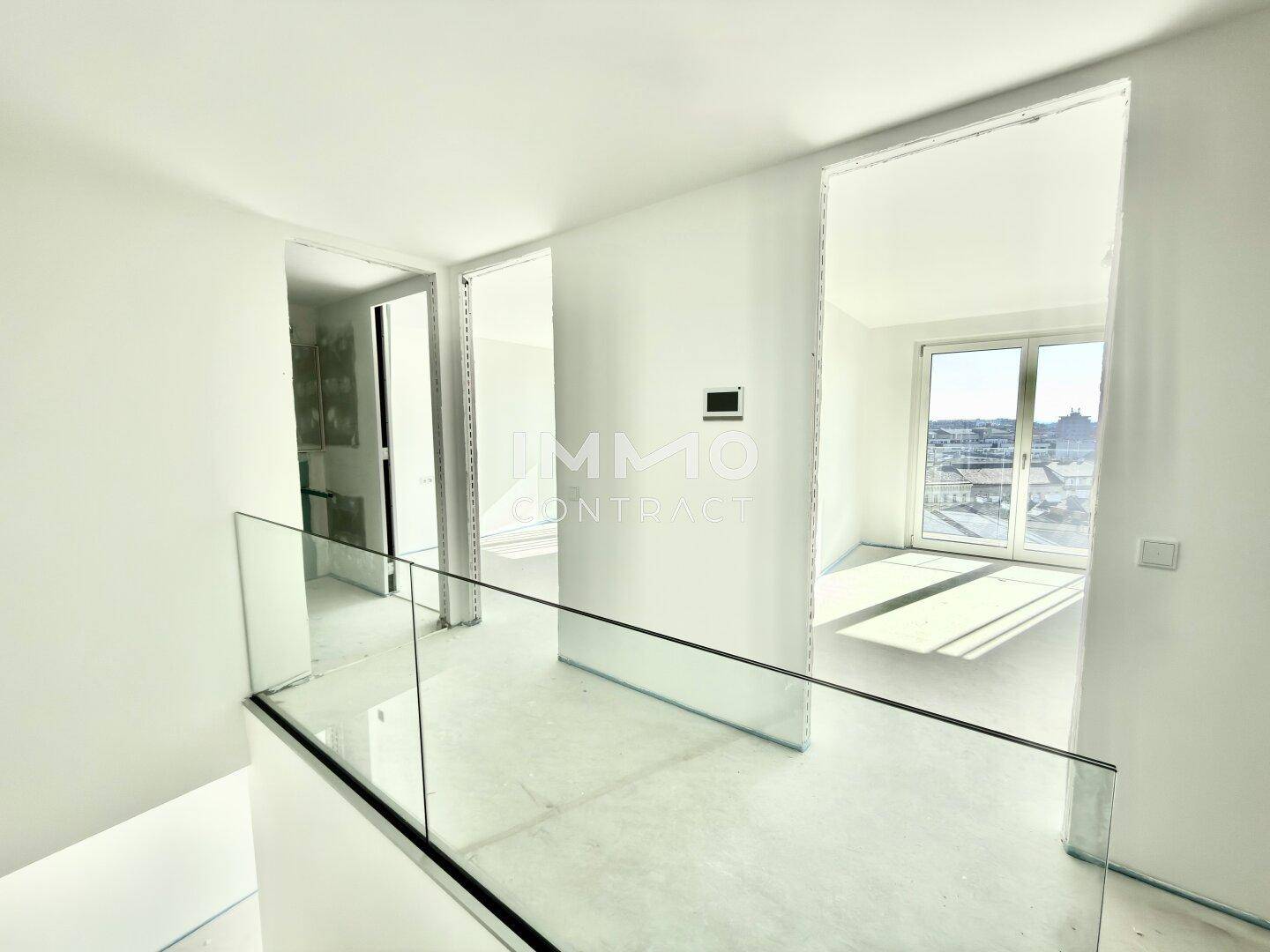 Heller Flurbereich mit moderner Glasbrüstung und Blick in angrenzende Räume mit großen Fenstern.