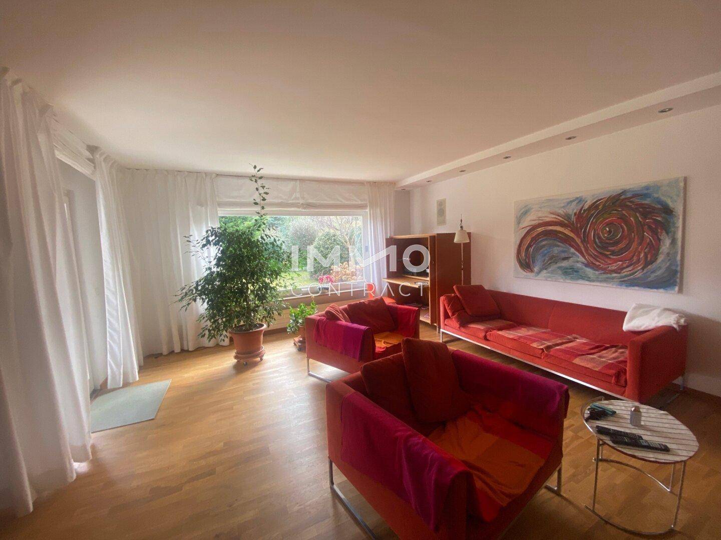 Helles Wohnzimmer mit farbenfrohen Sofas, Holzboden und großen Fenstern zum Garten.