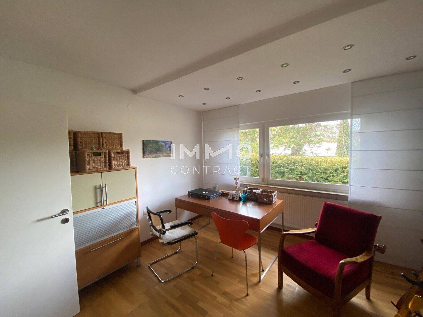 Helles Arbeitszimmer mit Schreibtisch, Stühlen und Blick in den grünen Außenbereich.