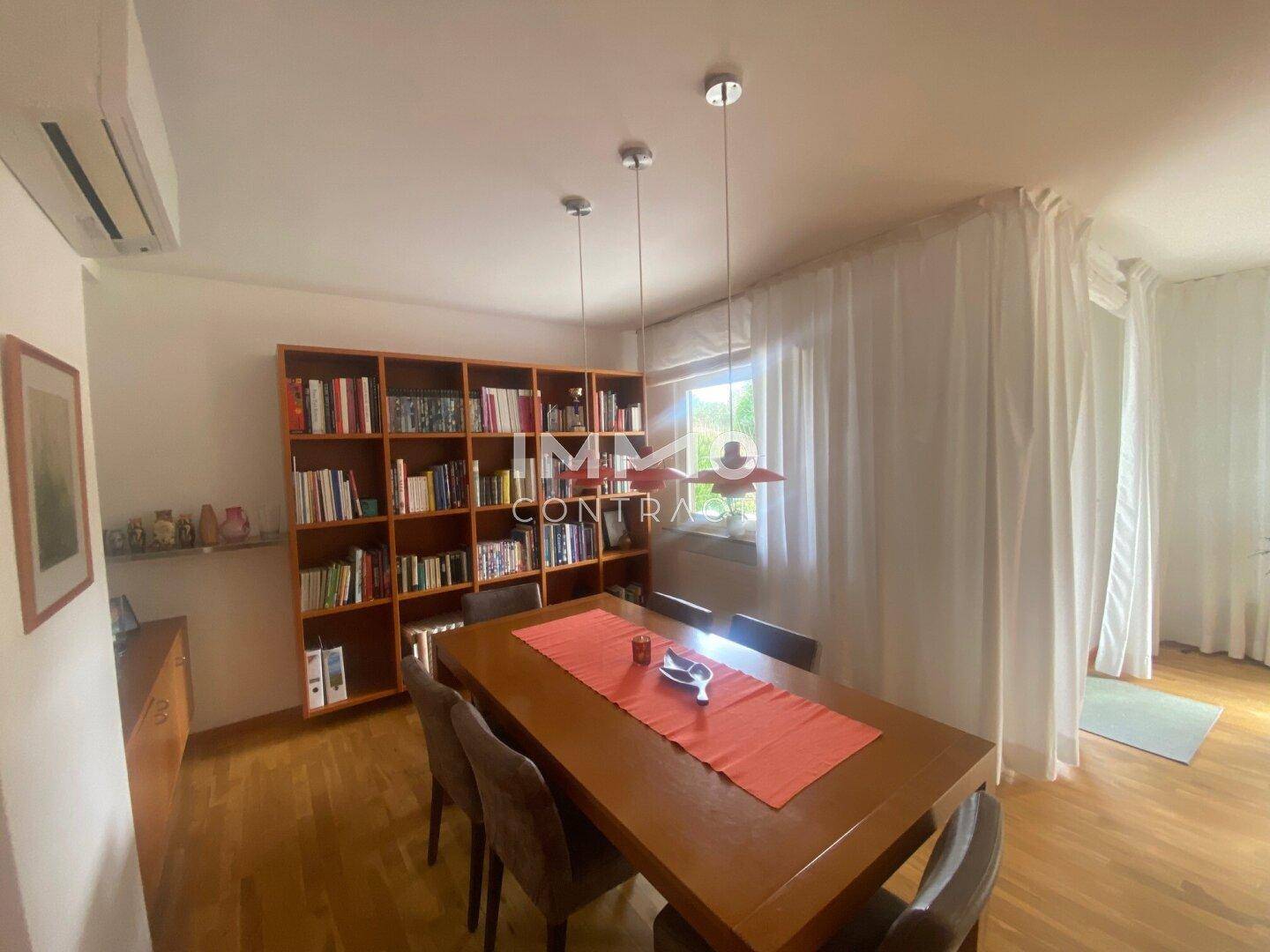Heller Essbereich mit Holztisch, Bücherregal und Klimaanlage für angenehmes Raumklima.