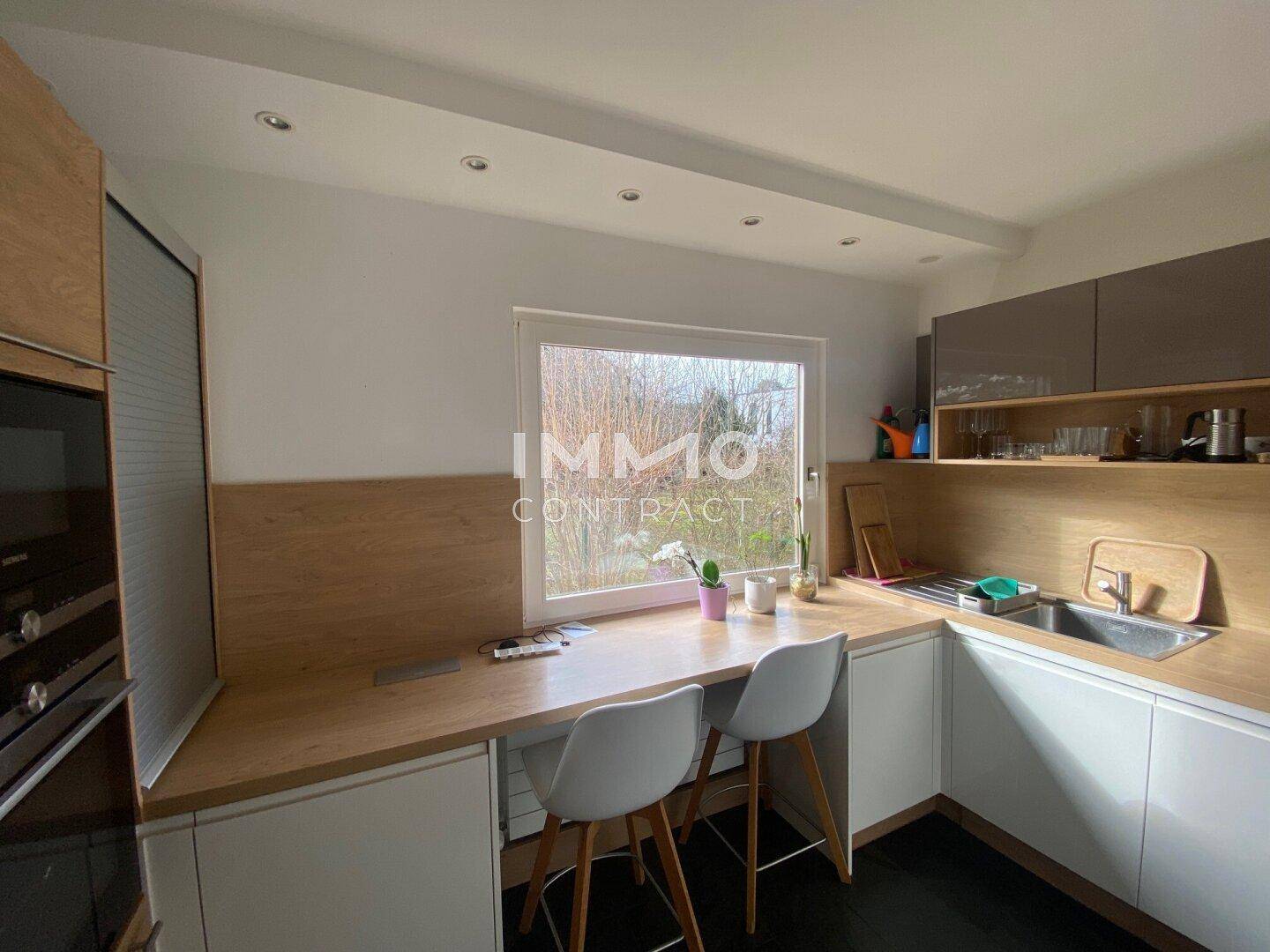 Moderne Küche mit Holzarbeitsplatten, weißen Unterschränken und integriertem Essbereich am Fenster.