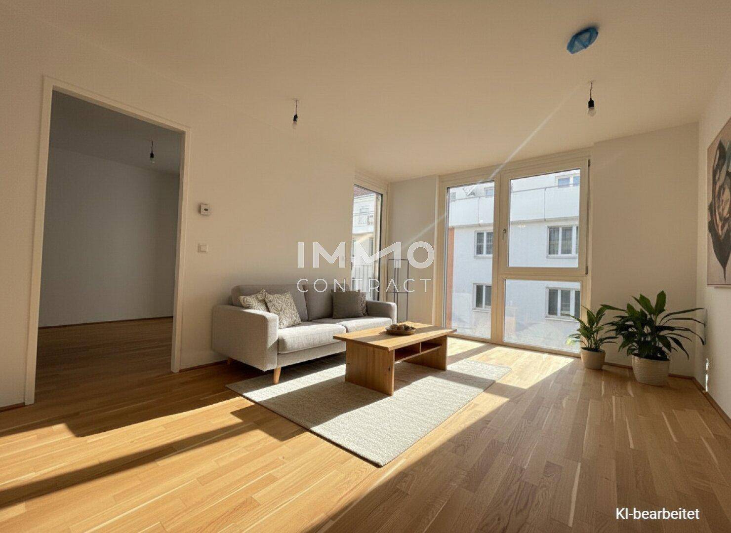Helles Wohnzimmer mit Parkettboden, großen Fenstern und Zugang zu einem weiteren Raum.