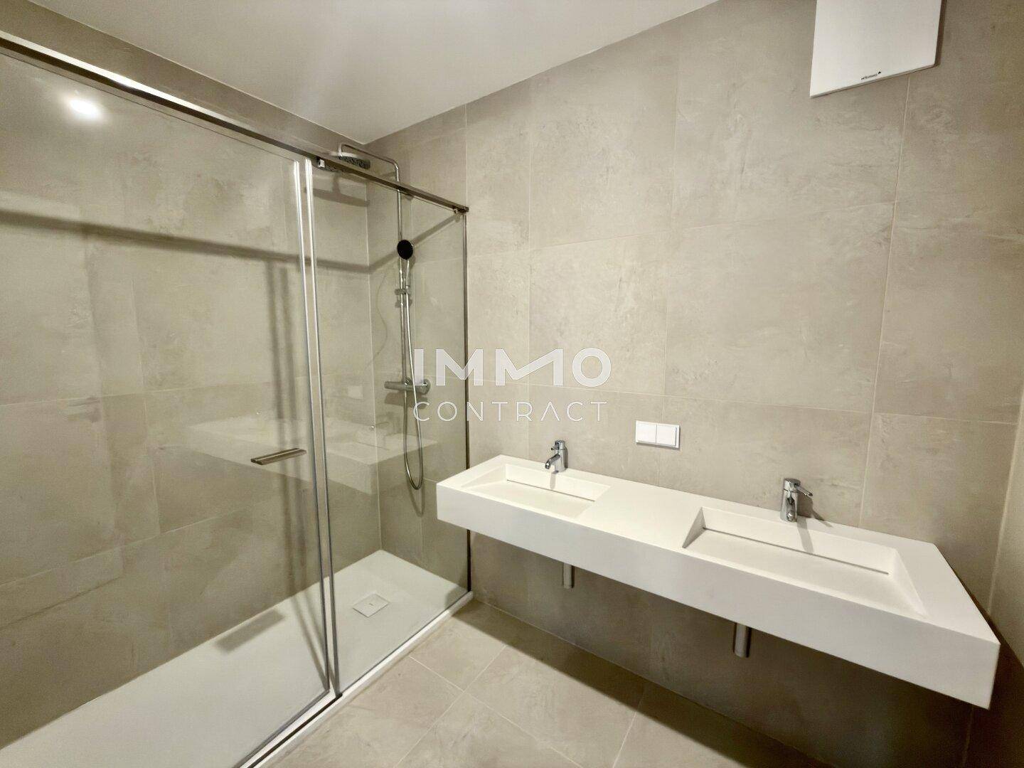 Modernes Badezimmer mit Doppelwaschbecken, großer begehbarer Dusche und hellen Fliesen.