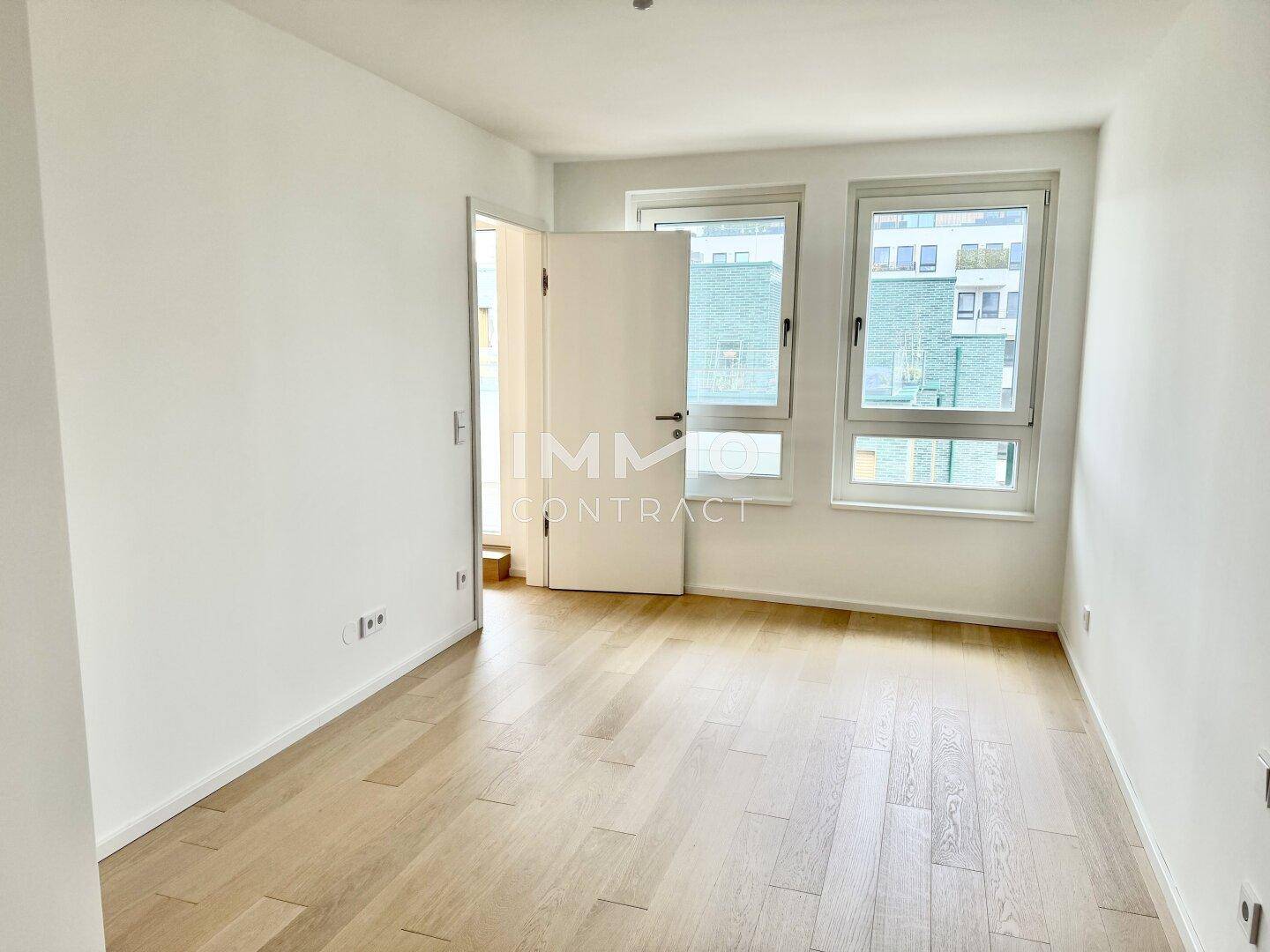Leeres Zimmer mit hellem Parkettboden und zwei Fenstern, ideal als Schlaf- oder Arbeitszimmer.