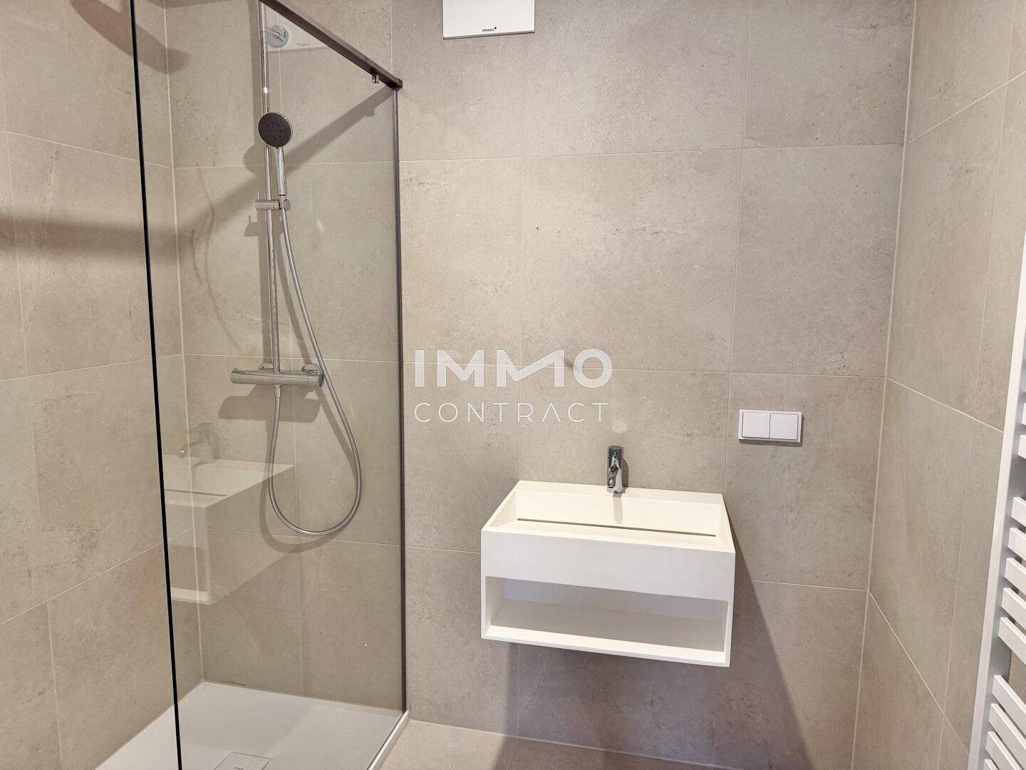 Modernes Badezimmer mit begehbarer Dusche, Wandwaschbecken und hellen Fliesen.