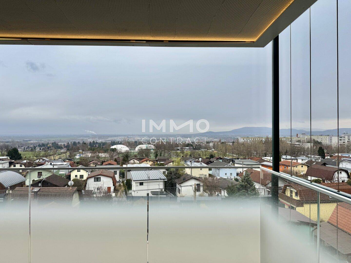 Balkon mit moderner Glasbrüstung und weitem Blick über die Dächer der Stadt und die Landschaft.