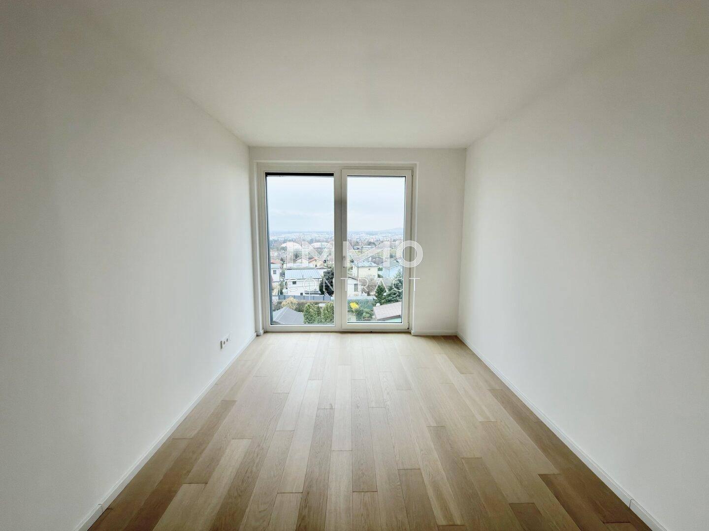 Leeres Schlafzimmer mit Holzboden und Fenster, das einen Blick auf die umliegende Bebauung bietet.