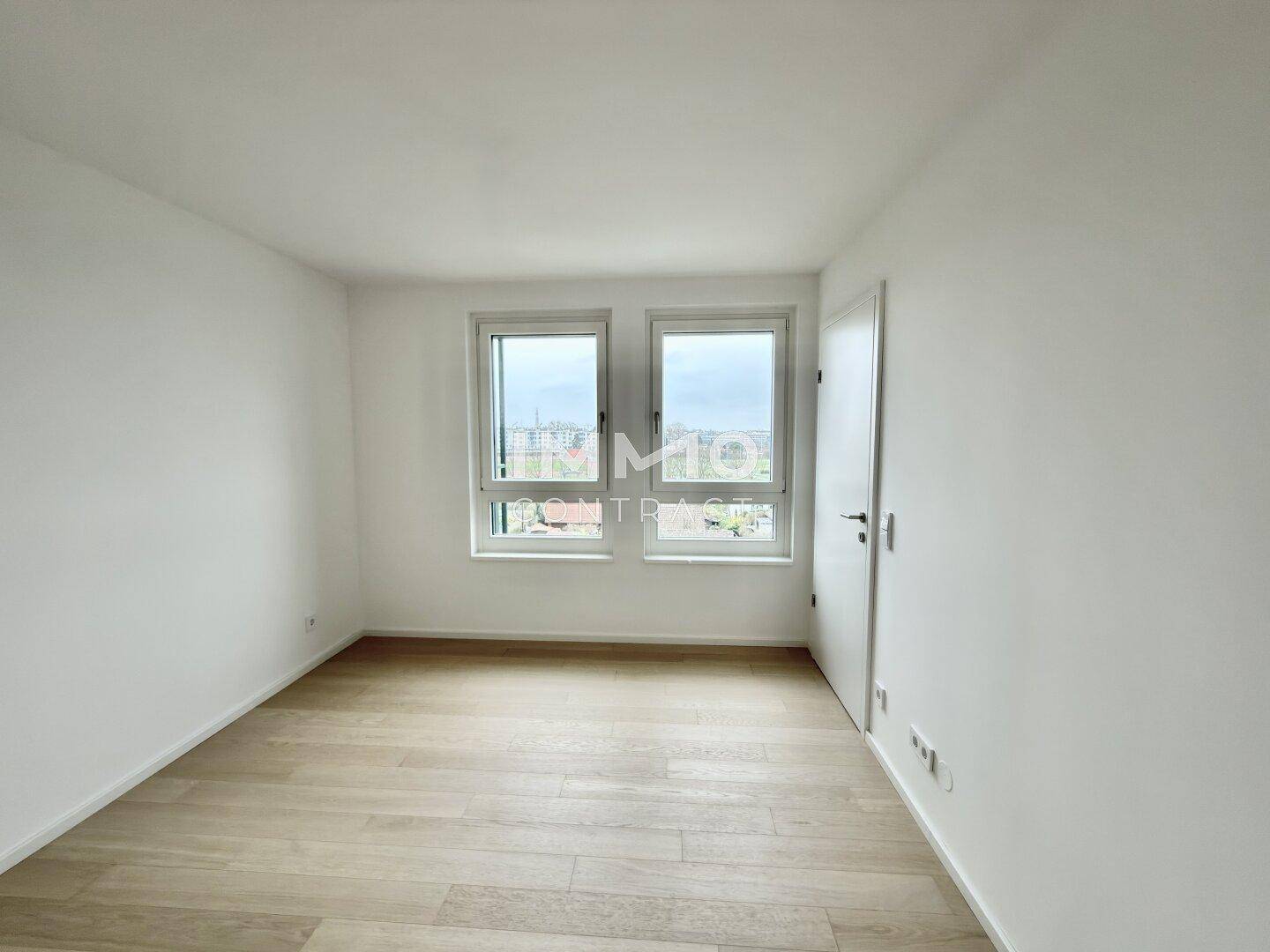 Helles Schlafzimmer mit Holzboden und zwei Fenstern, die einen Blick auf die Umgebung bieten.