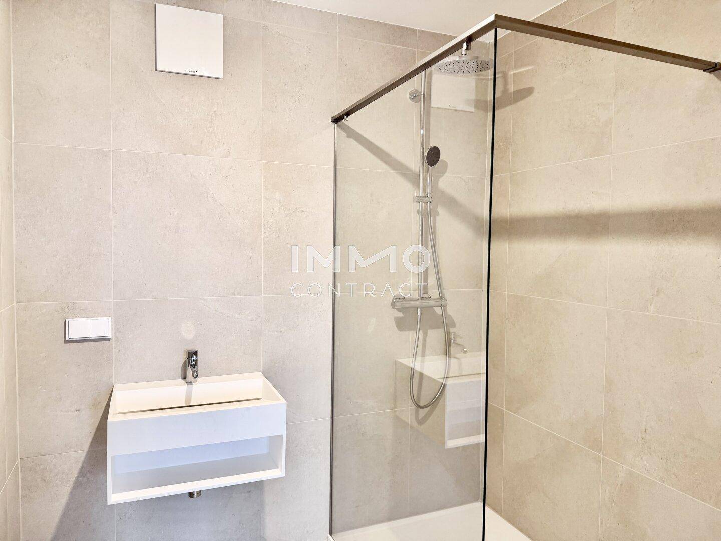 Modernes Badezimmer mit großer Duschkabine, Wandwaschbecken und hellen Fliesen.