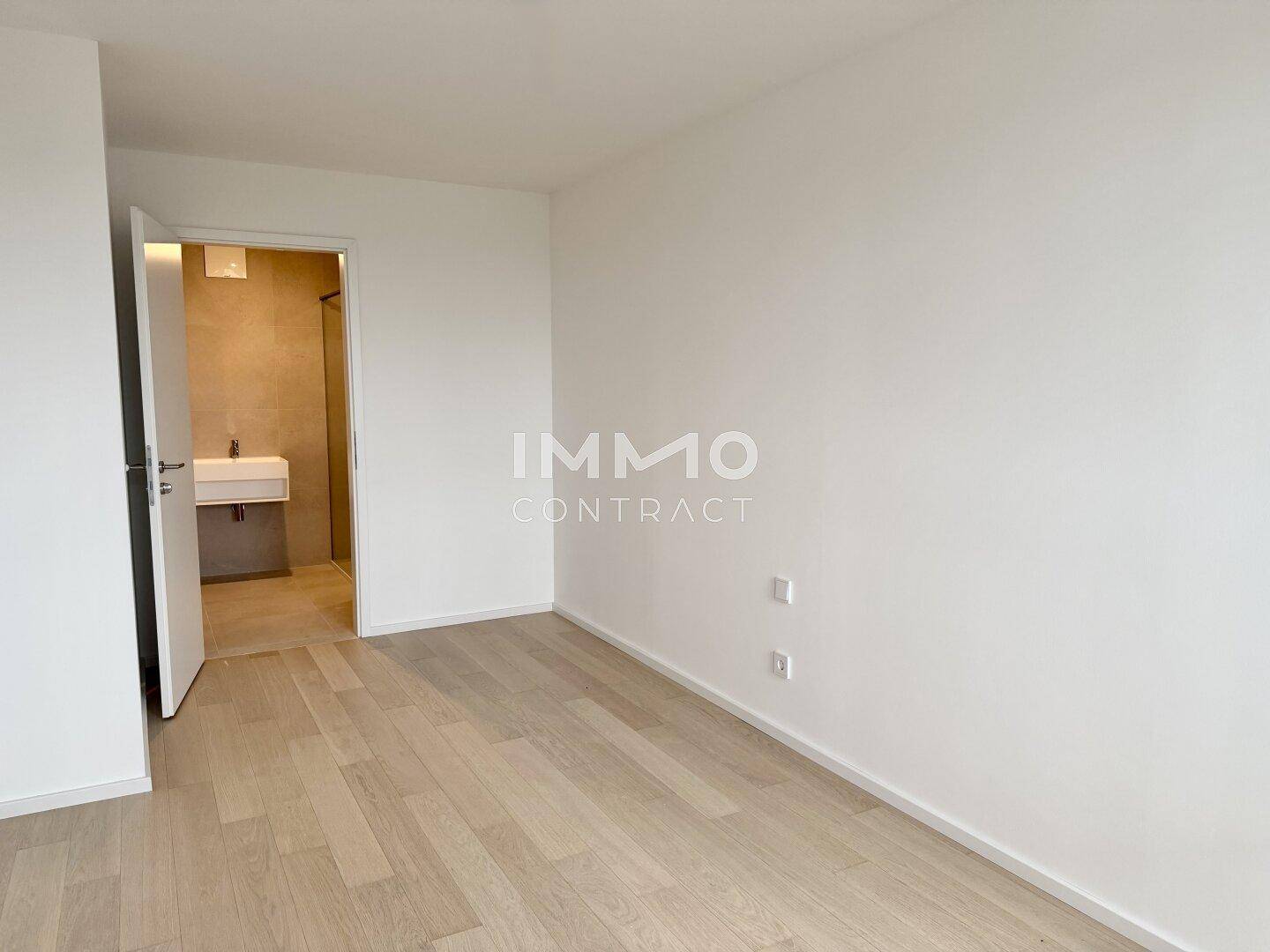 Schlafzimmer mit hellem Parkettboden und direktem Zugang zu einem modernen Badezimmer.
