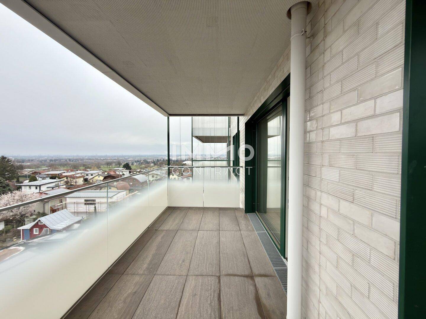 Moderner Balkon mit Glasbrüstung und Fliesenboden, bietet weite Aussicht.
