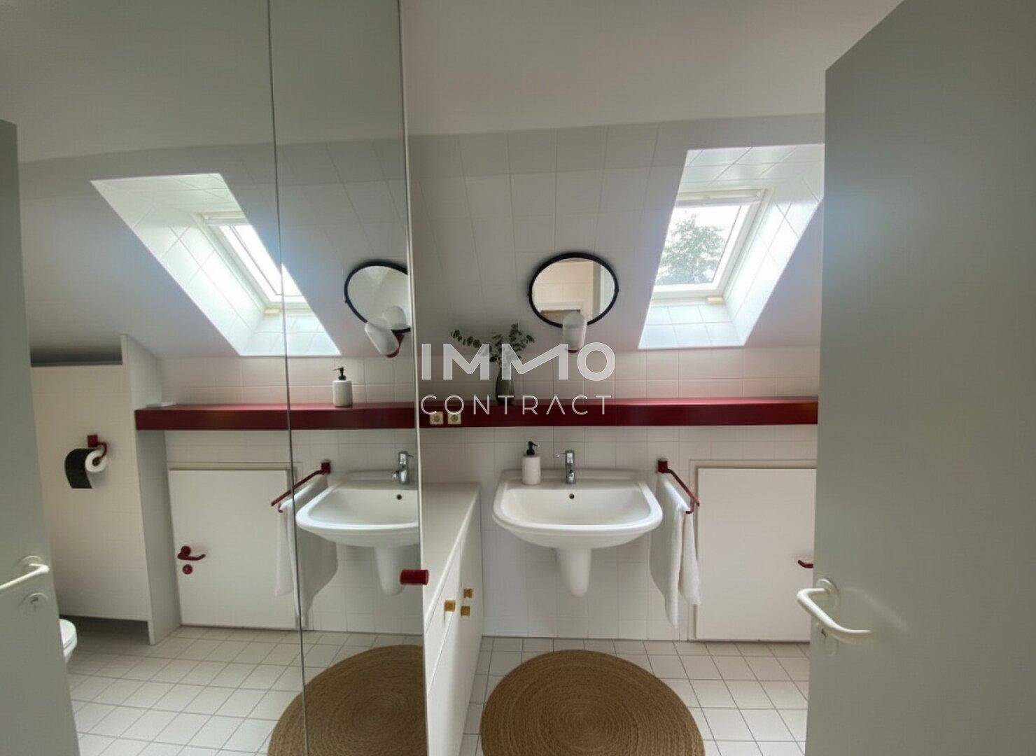 Badezimmer im Dachgeschoss mit Doppelwaschbecken, Dachfenstern und Fliesenboden.