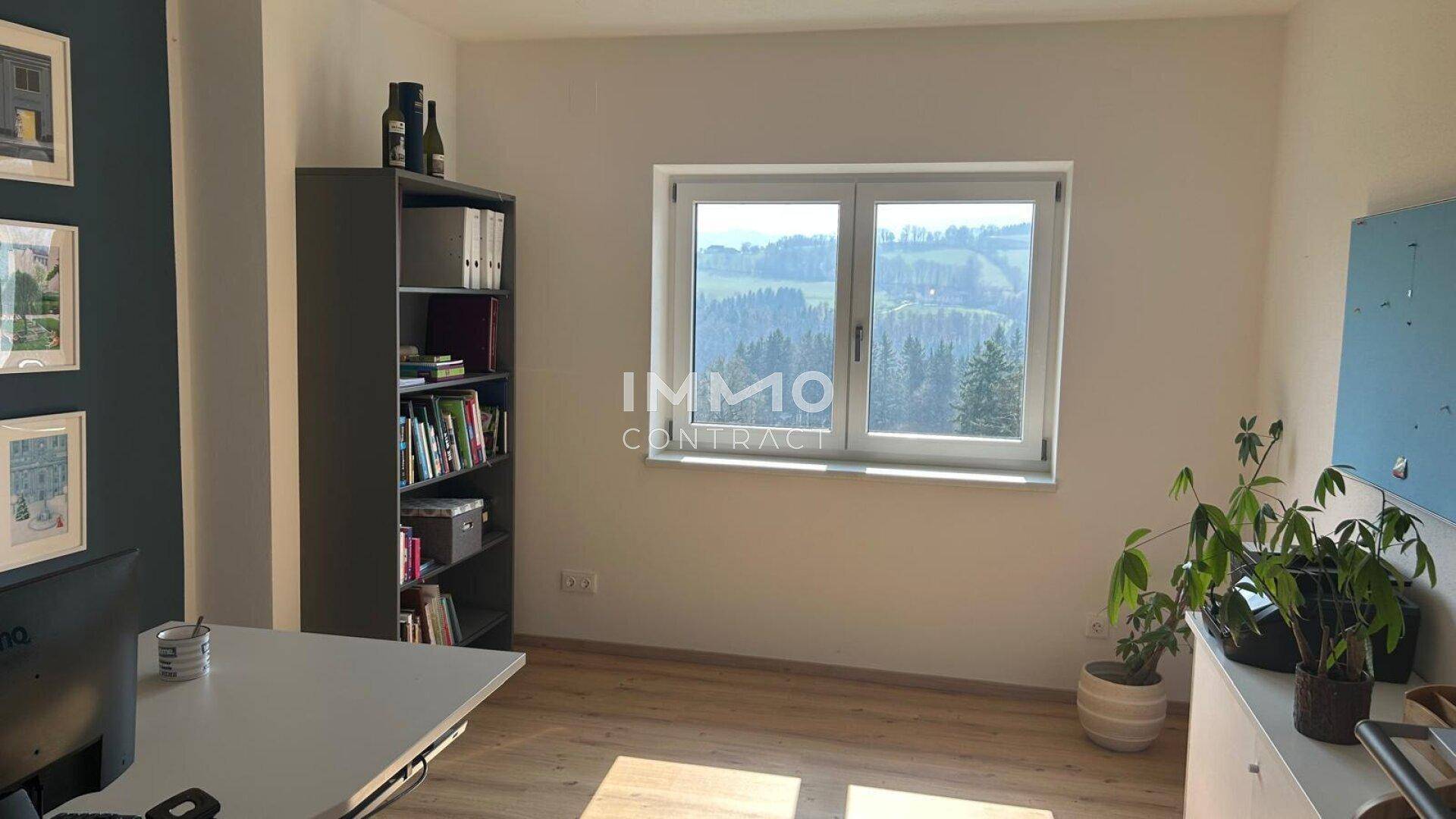 Helles Arbeitszimmer mit großem Fenster, Blick ins Grüne und modernem Schreibtisch.