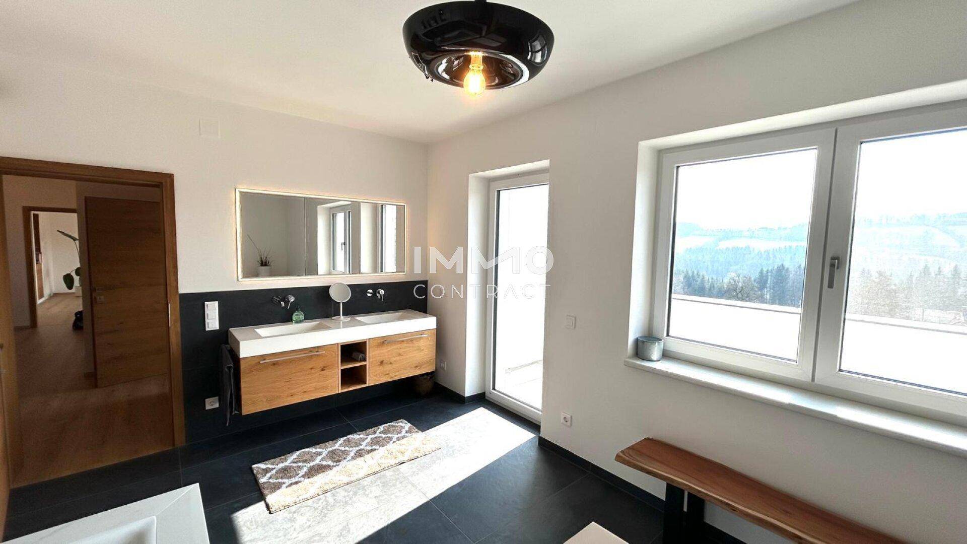 Modernes Badezimmer mit Doppelwaschbecken, dunklen Fliesen und Zugang zum Balkon.