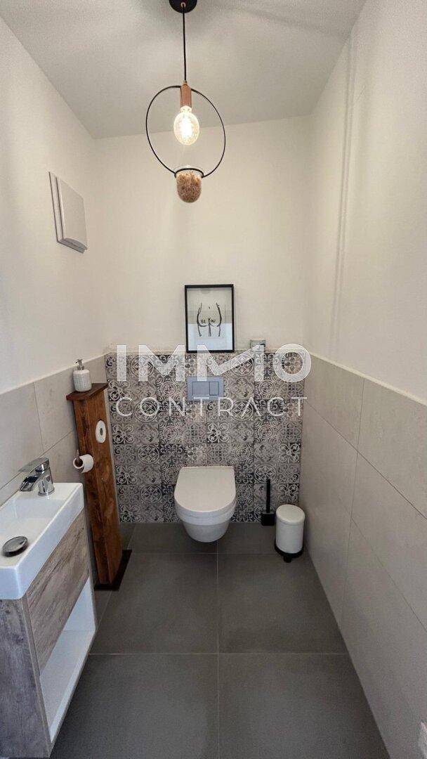 Modernes Gäste-WC mit Wand-WC, kleinem Waschbecken und dekorativen Fliesen.