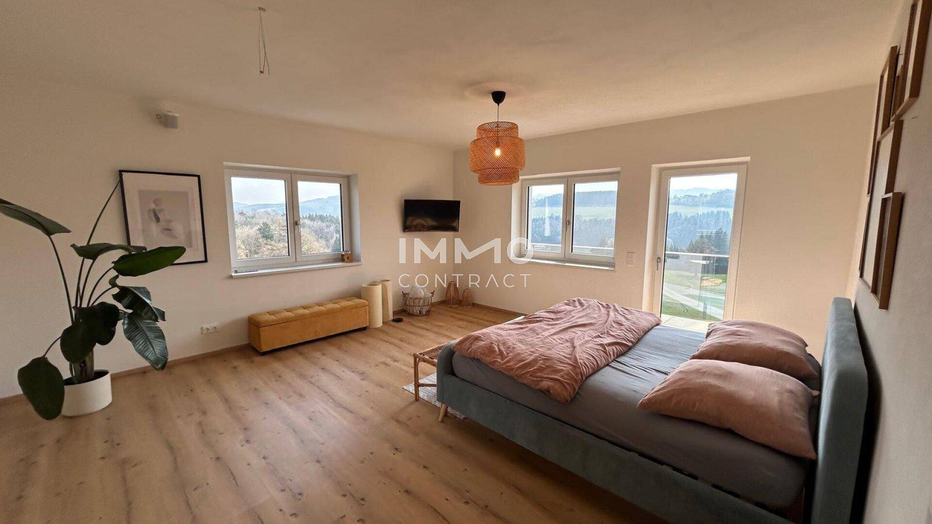 Geräumiges Schlafzimmer mit Holzboden, großem Bett und Fenstern mit Blick ins Grüne.