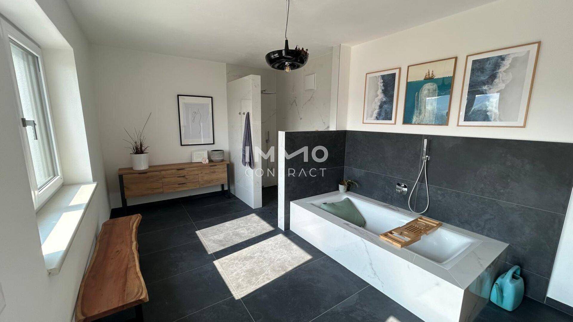 Geräumiges Badezimmer mit moderner Badewanne, dunklen Fliesen und Kunstwerken an der Wand.