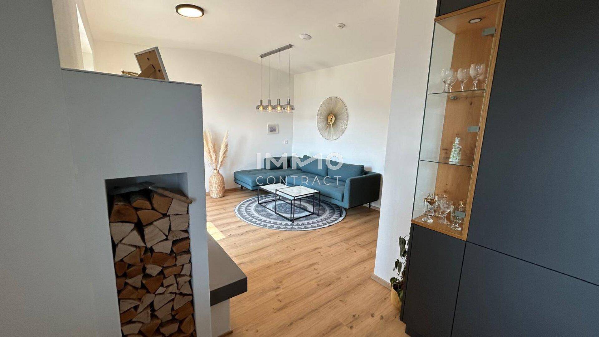 Heller Wohnbereich mit Kamin, Holzstapel und Blick auf das gemütliche Sofa.