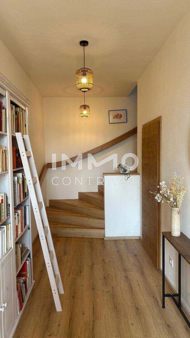 Heller Flur mit eingebauten Bücherregalen, Holztreppe und moderner Beleuchtung.
