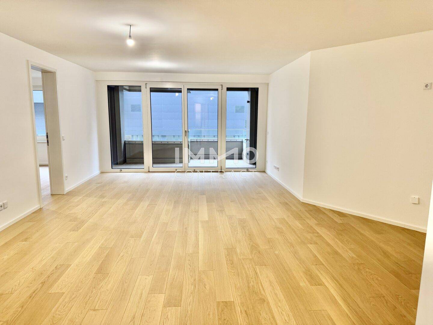 Heller Wohnbereich mit Parkettboden und Zugang zu einem Balkon durch große Glastüren.