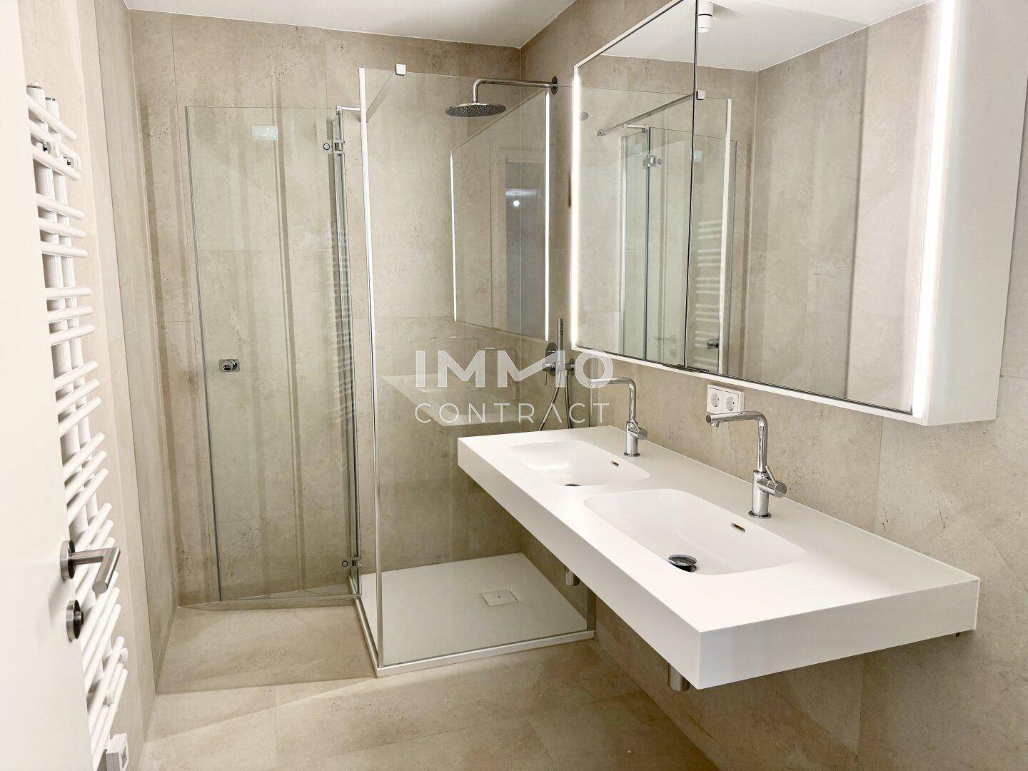 Modernes Badezimmer mit Doppelwaschbecken, begehbarer Dusche und beheiztem Handtuchhalter.