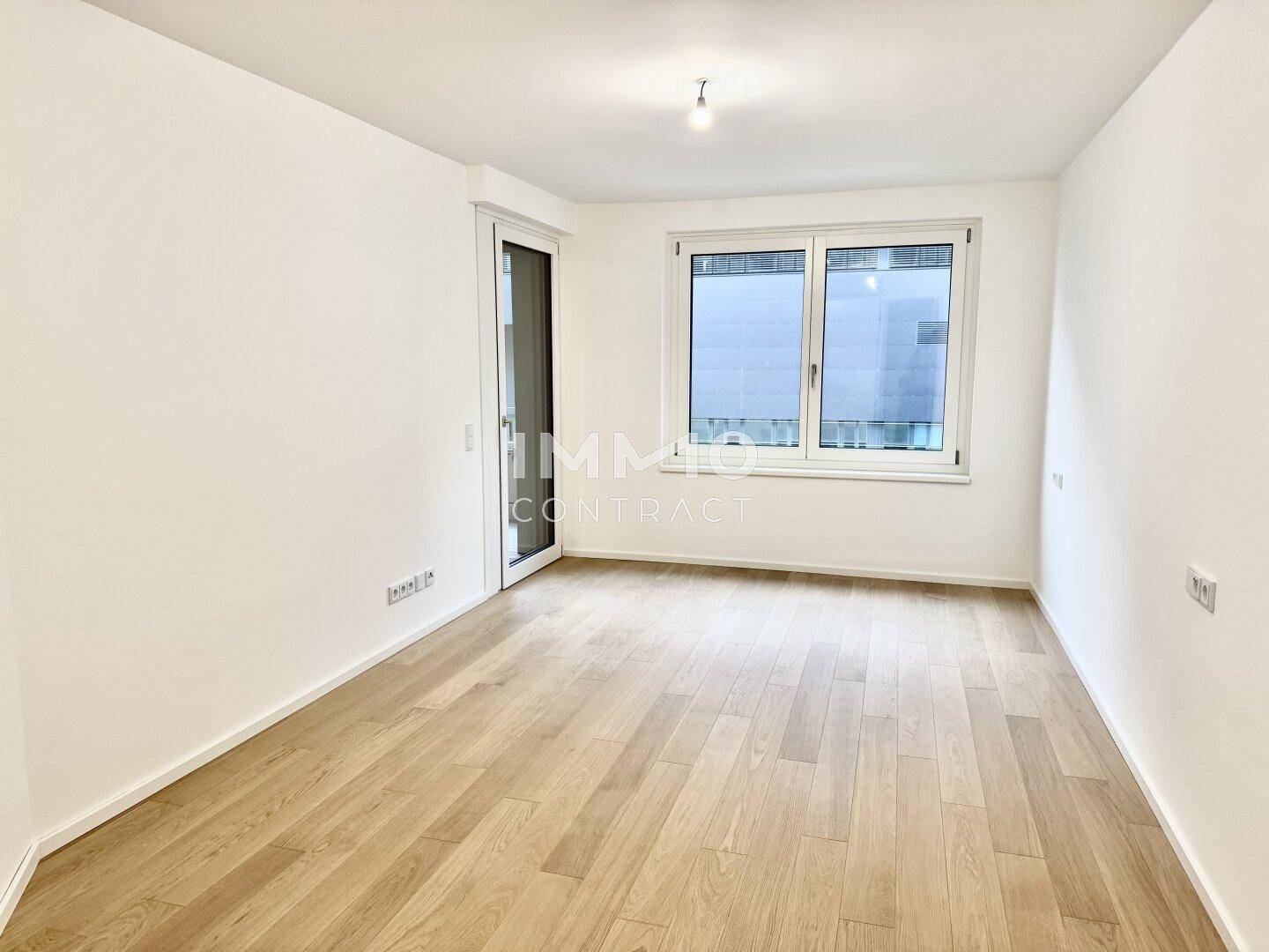 Helles Zimmer mit Holzboden und großem Fenster, das viel Tageslicht hereinlässt.
