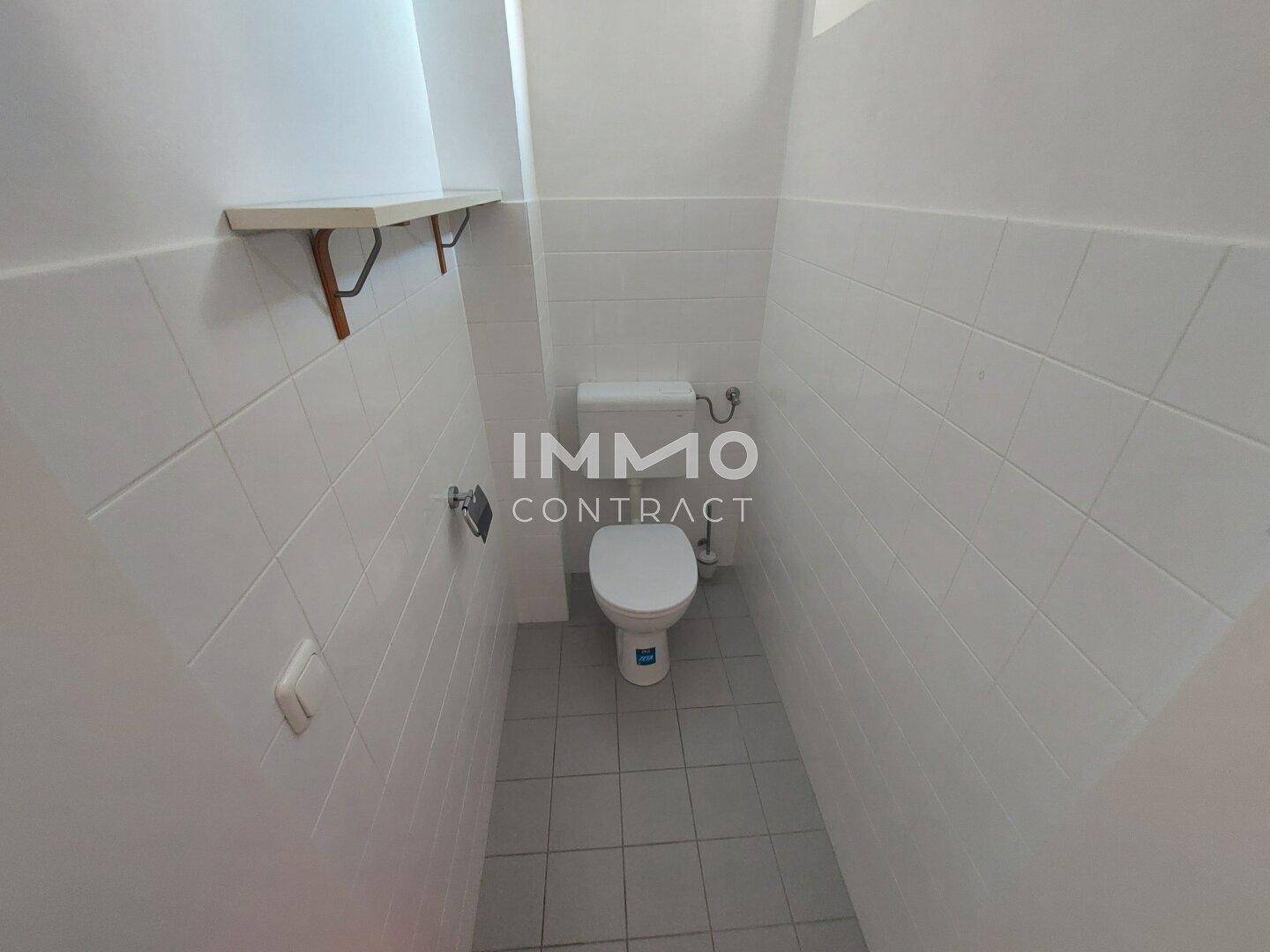 Separate Toilette mit weißen Fliesen und einfachem WC.
