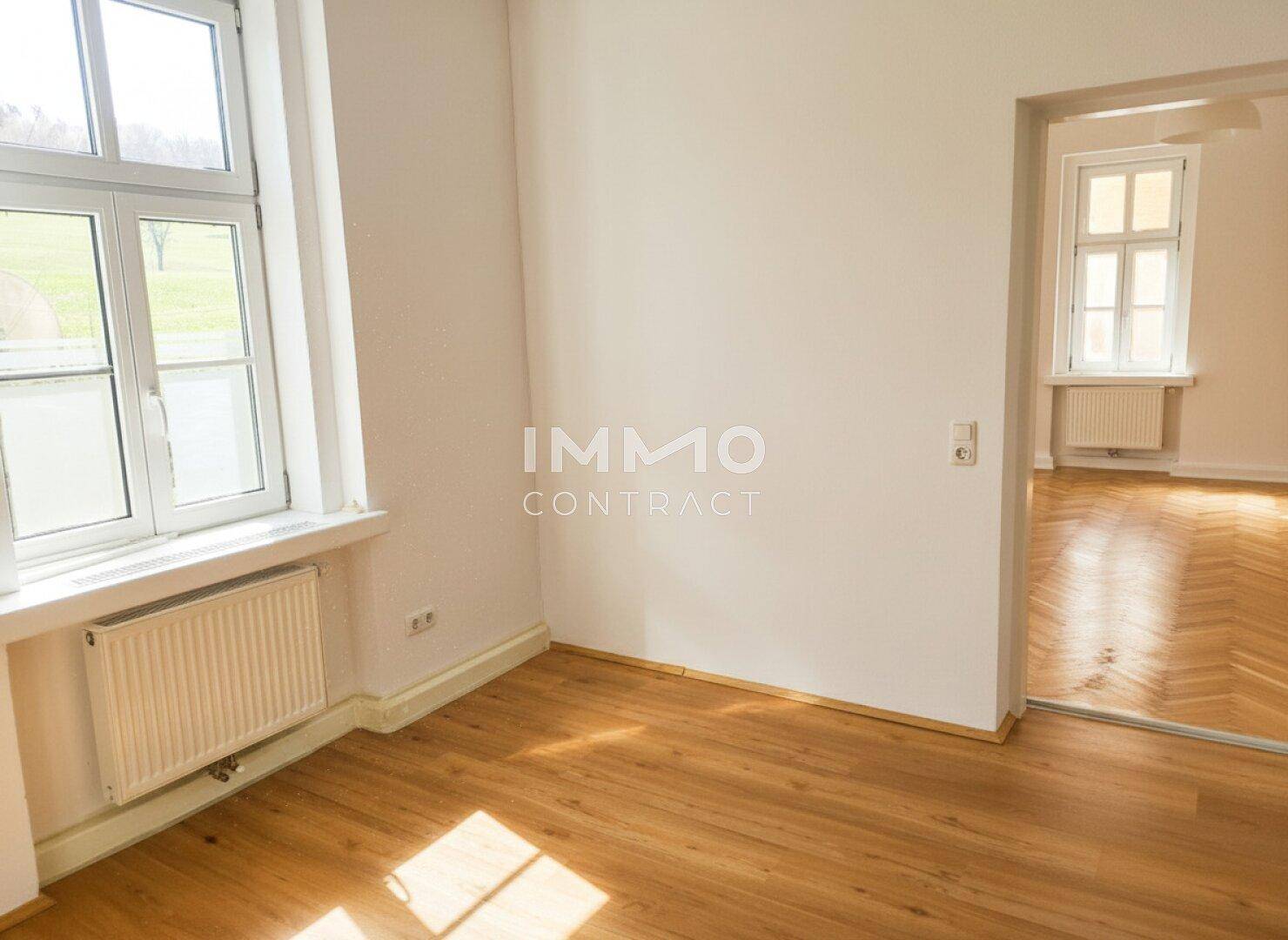 Helles Zimmer mit Laminatboden und Zugang zu einem weiteren Raum.