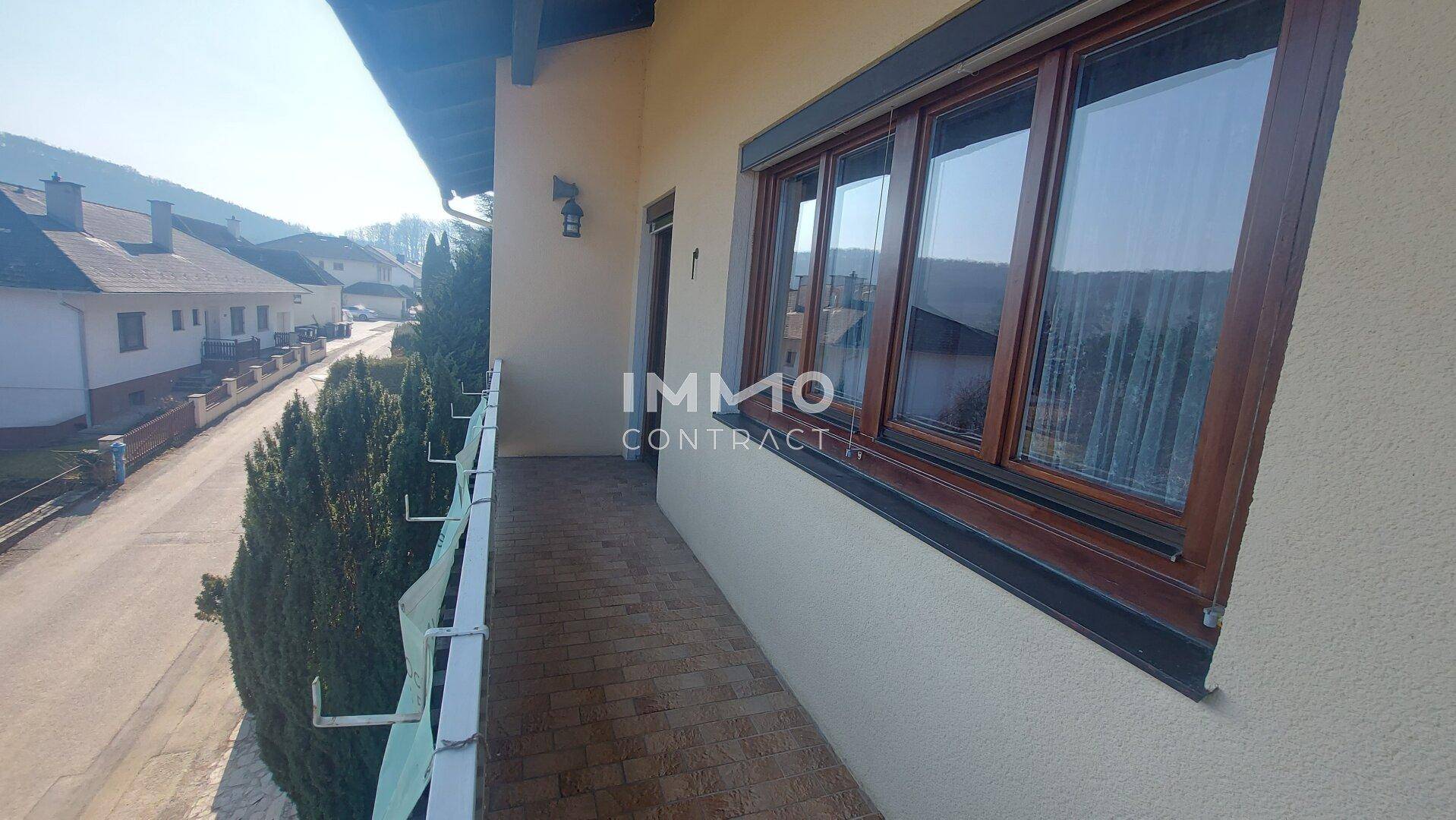 Langer Balkon mit Fliesenboden und Blick auf die Straße und die umliegende Wohngegend.