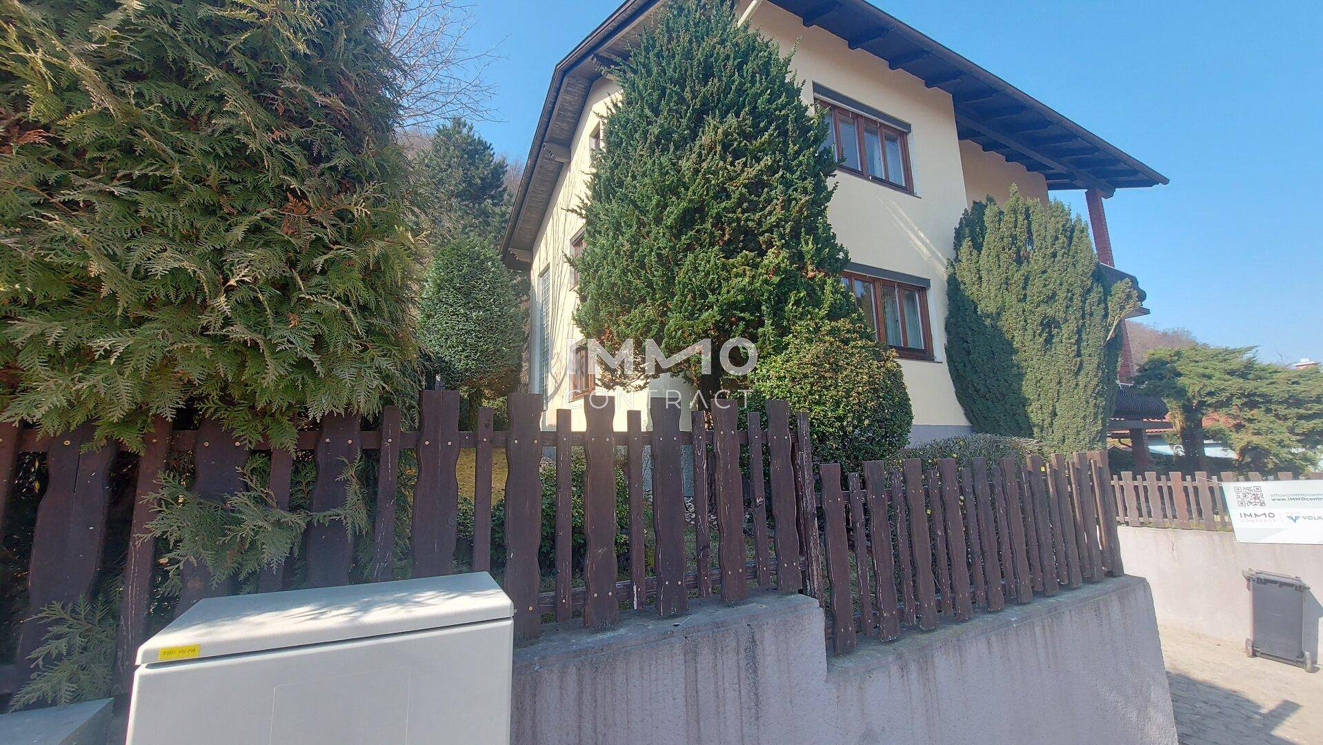 Vorderansicht eines Einfamilienhauses mit gepflegter Hecke und Holzzaun an einem sonnigen Tag.