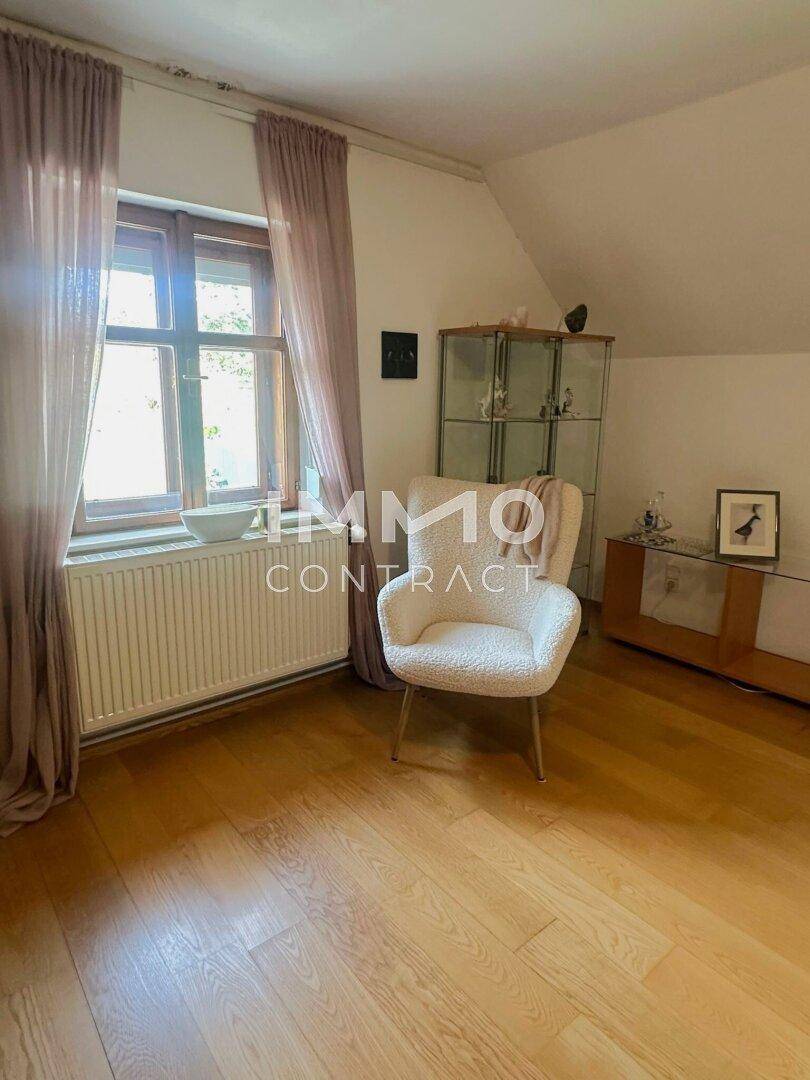 Helles Schlafzimmer mit Holzboden, einem Fenster und einem gemütlichen Sessel, unter einem leicht schrägen Dach.
