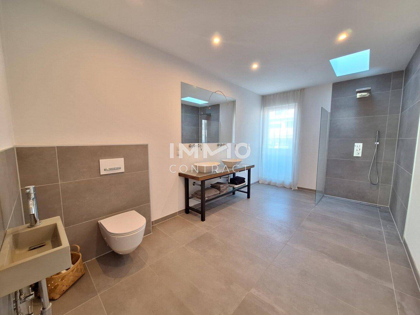 Großes modernes Badezimmer mit Doppelwaschbecken, begehbarer Dusche und Wand-WC.