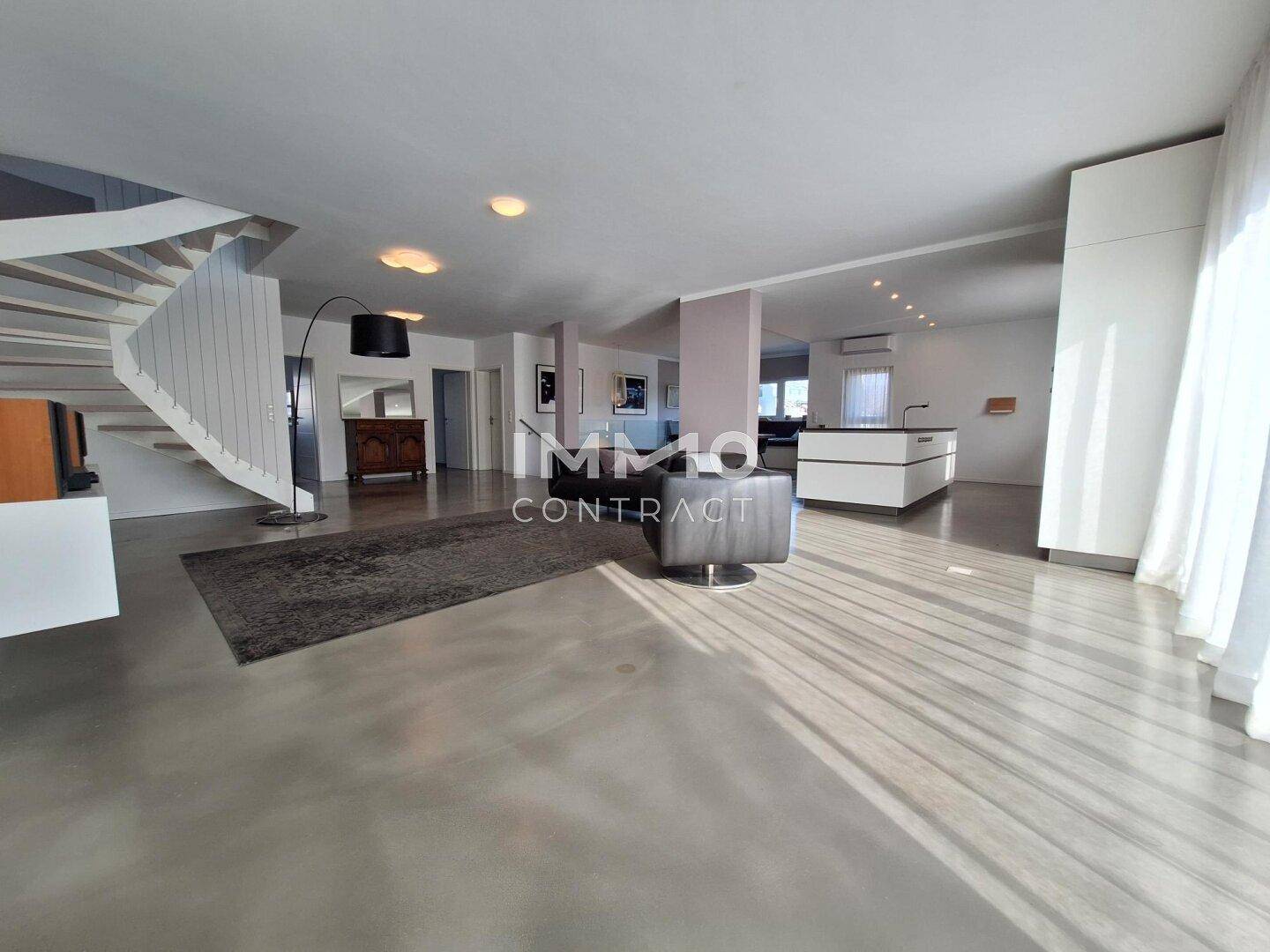 Geräumiger offener Wohnbereich mit moderner Treppe, Betonboden und viel Tageslicht.