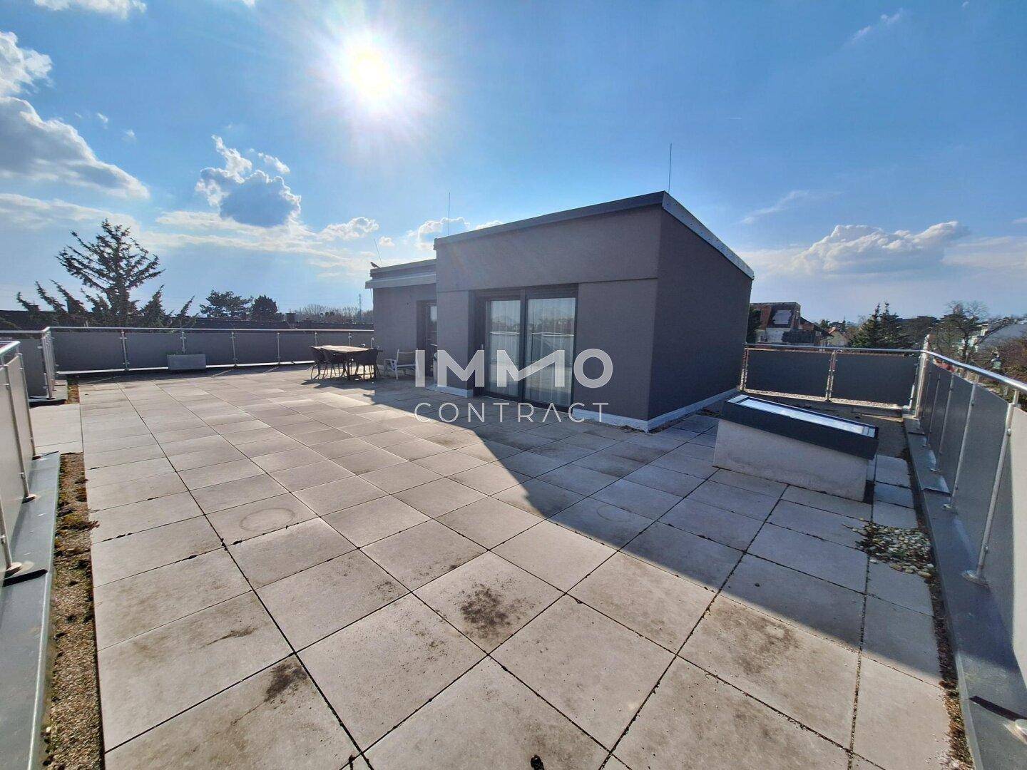 Große Dachterrasse mit Fliesenboden und weitem Blick unter blauem Himmel.
