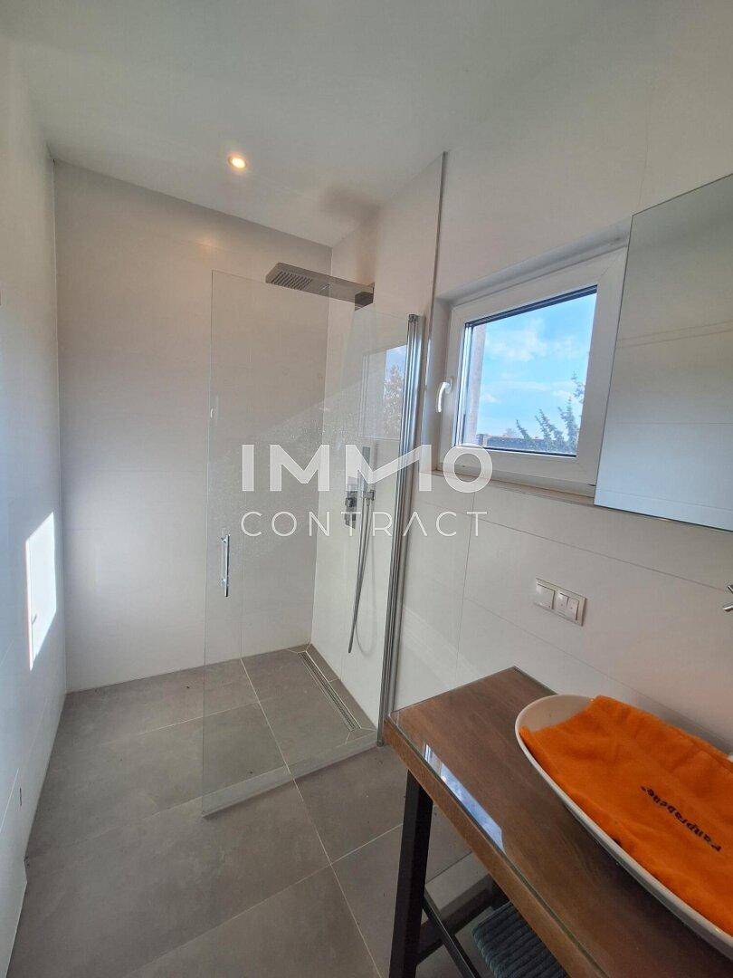 Geräumige begehbare Dusche mit Glasabtrennung und Fenster im modernen Badezimmer.