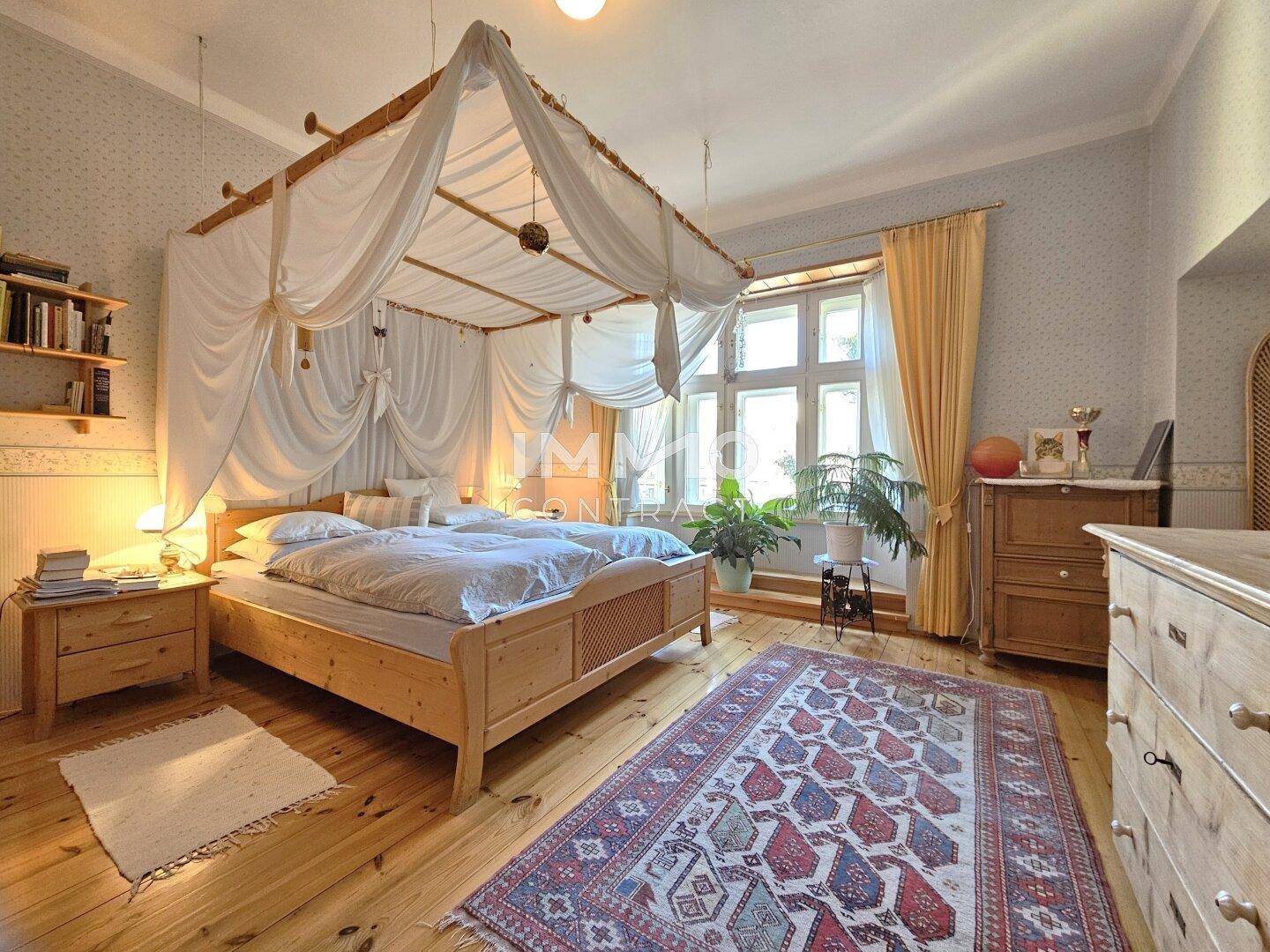 Helles Schlafzimmer mit Himmelbett, Holzfußboden und großen Fenstern.