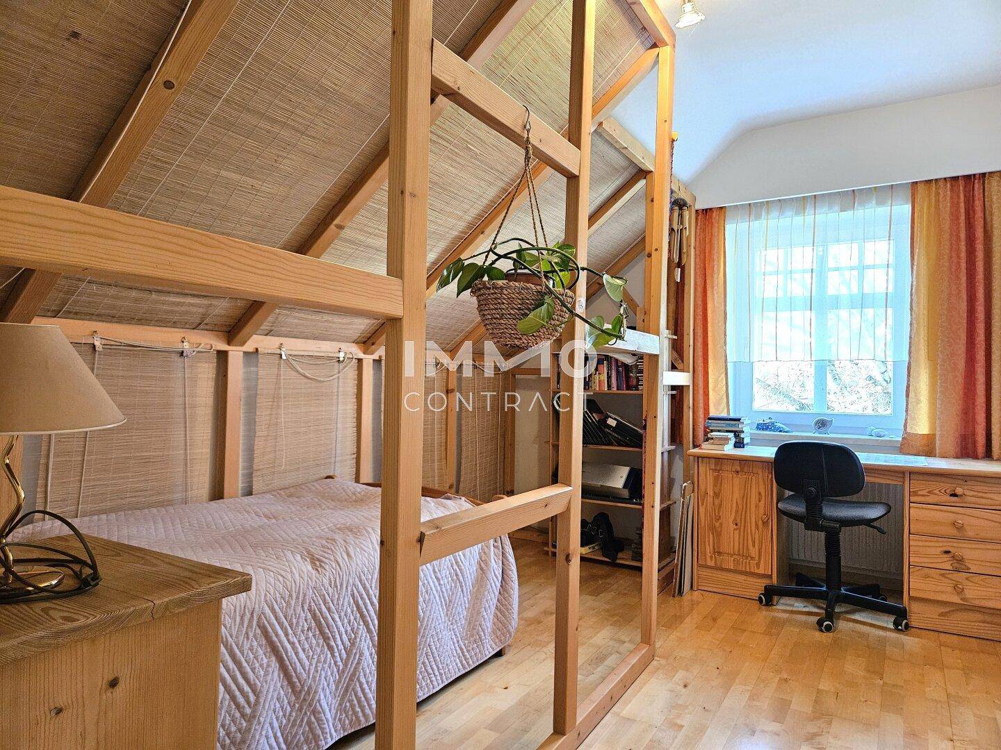 Schlafzimmer im Dachgeschoss mit Holzbett, Schreibtisch und Fenster.