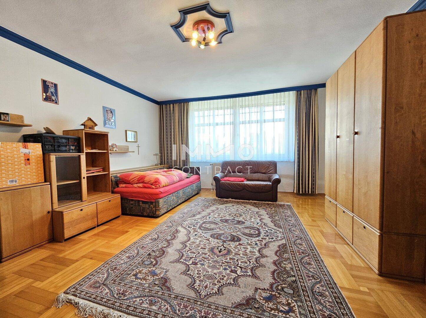 Geräumiges Schlafzimmer mit großem Teppich, Schränken und Fensterfront.