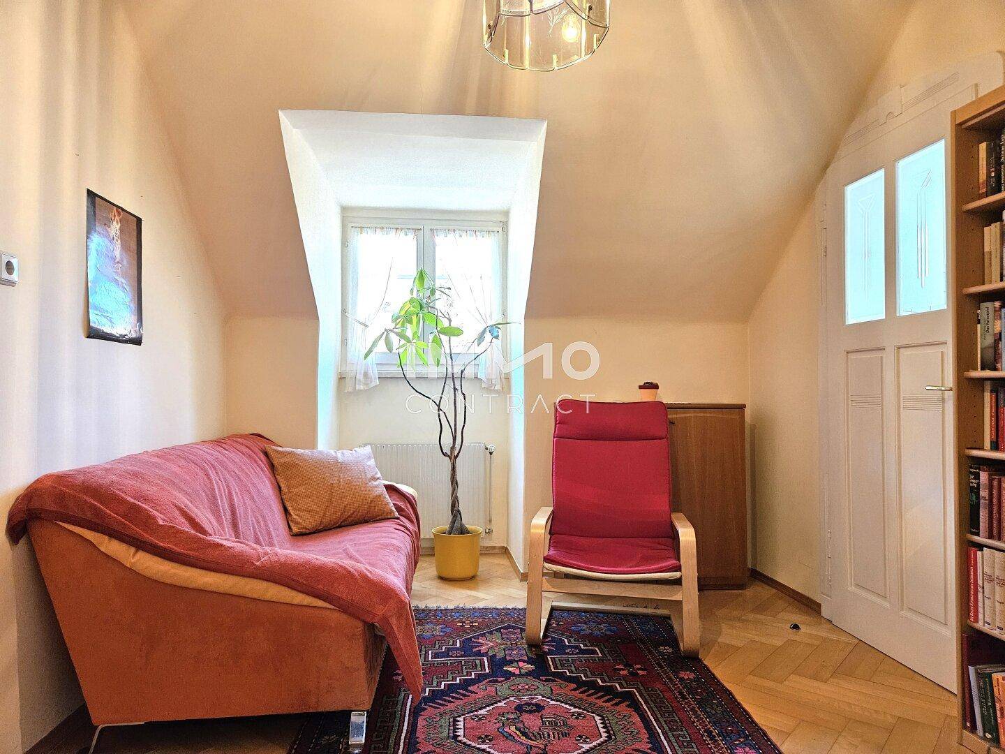 Gemütliches Dachzimmer mit Sofa, Sessel und Fenster, ideal als Rückzugsort.